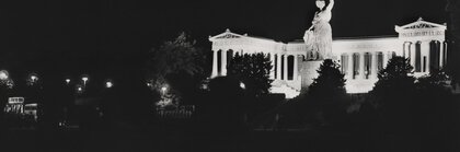 Black and white photo of the Bavaria statue at night, the laurel wreath in the statue's hand is illuminated by a laser and is brightly lit.