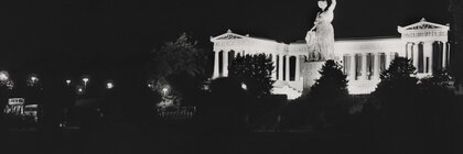 Black and white photo of the Bavaria statue at night, the laurel wreath in the statue's hand is illuminated by a laser and is brightly lit.