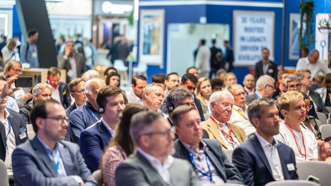 Many people are sitting on chairs and listening to a presentation on stage at Transport Logistic 2025.