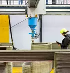 A person in safety clothing monitors a 3D printer producing a concrete structure.