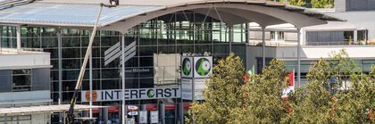 Entrance area of Messe München with INTERFORST signage, glass facade and solar panels on the exhibition hall roofs.