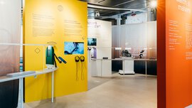 An exhibition stand at INHORGENTA with a long winding table displaying exhibits on the theme of watchmaking and several large colourful information walls.
