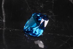 Ein großer, facettierter blauer Edelstein auf einer reflektierenden schwarzen Oberfläche.