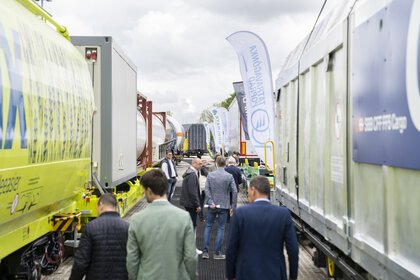 Visitors to transport logistic on the open-air site of Messe München between two rows of colourful railway wagons.
