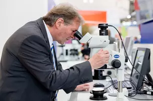 A man in a suit looks through a microscope at an exhibition stand.