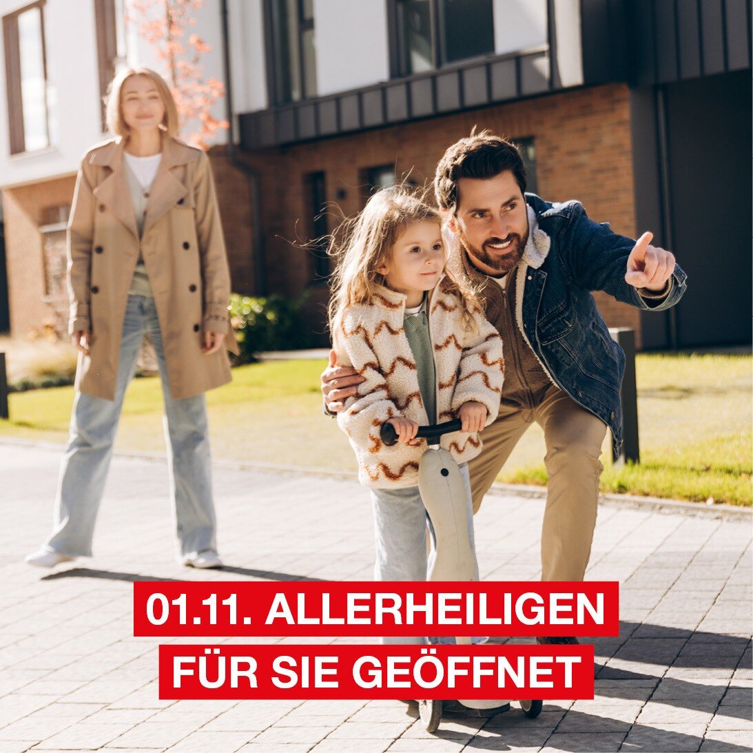 Eine Frau, ein Mann und ein kleines Mädchen auf einem Tretroller stehen vor einigen Wohnhäusern und schauen lächelnd in die Ferne.