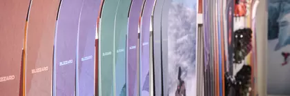 Bunte Skier stehen vertikal aufgereiht an einer Ausstellerwand, im Hintergrund sind Skiausrüstung und Bergfotos zu sehen.