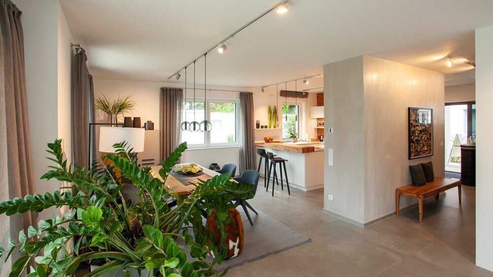 Moderner offener Wohnraum mit Essbereich, Küche und großen Grünpflanzen am Fenster.