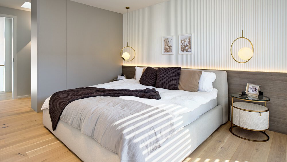 Modernes Schlafzimmer mit großem Bett, weißer und grauer Bettwäsche, runden Nachttischen und Hängelampen auf hellem Holzboden.