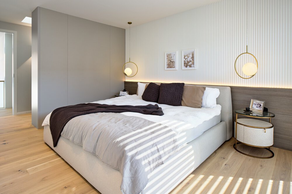Modernes Schlafzimmer mit großem Bett, weißer und grauer Bettwäsche, runden Nachttischen und Hängelampen auf hellem Holzboden.