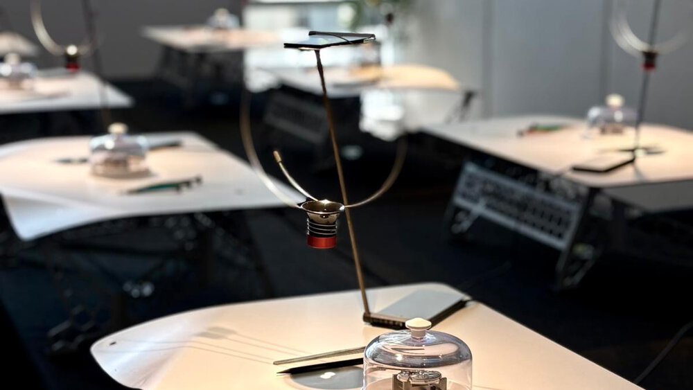 Several identical metal work tables with rounded corners, with table lamps and watchmaker's tools on them.
