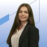Junge Frau mit langen braunen Haaren in weißer Bluse und schwarzem Blazer vor modernem, blauem Hintergrund mit geometrischen Formen.