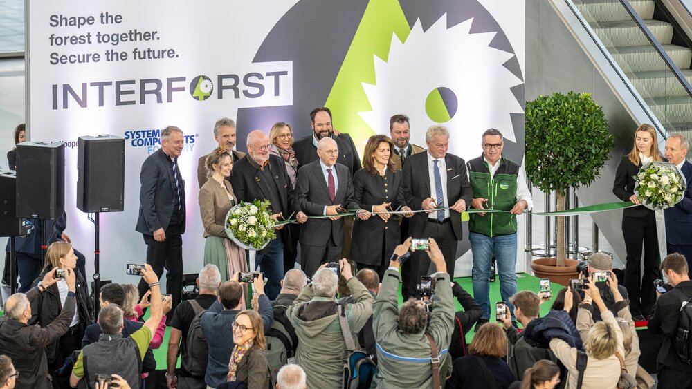 Several people cutting a green ribbon in front of an exhibition backdrop as the audience takes photos.