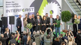 Several people cutting a green ribbon in front of an exhibition backdrop as the audience takes photos.