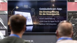 Menschen mit Kopfhörern nehmen an einer geführten Tour teil und Blicken auf einen Screen, der eine Gebäude-Scan-App erläutert.