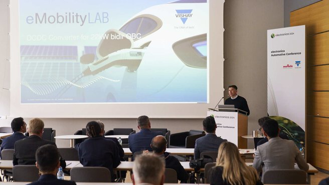 A person speaks from a podium in a conference room and presents a slide about eMobility.