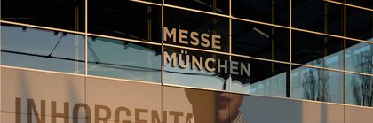 Reflection of a building on the glass façade of the Munich Trade Fair Centre with an INHORGENTA advertisement.