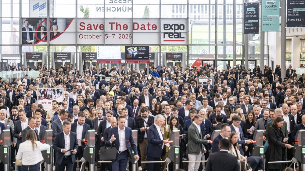 Eine große Menschenmenge betritt ein Kongresszentrum für die Expo Real, mit einem Banner, das die Veranstaltungstermine im Oktober 2026 anzeigt.
