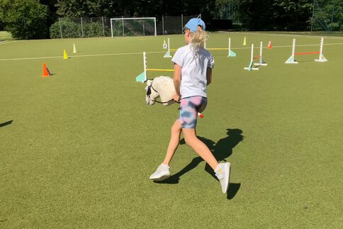 Ein Mädchen springt mit einem FABLEHORSE Hobby Horse über ein Hindernis. Das Bild zeigt Hobby Horsing als sportliche Freizeitaktivität und passt zur Podcast-Folge über FABLEHORSE auf der f.re.e.
