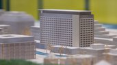 Close-up of an architectural model with focus on a modern high-rise surrounded by smaller buildings and trees.