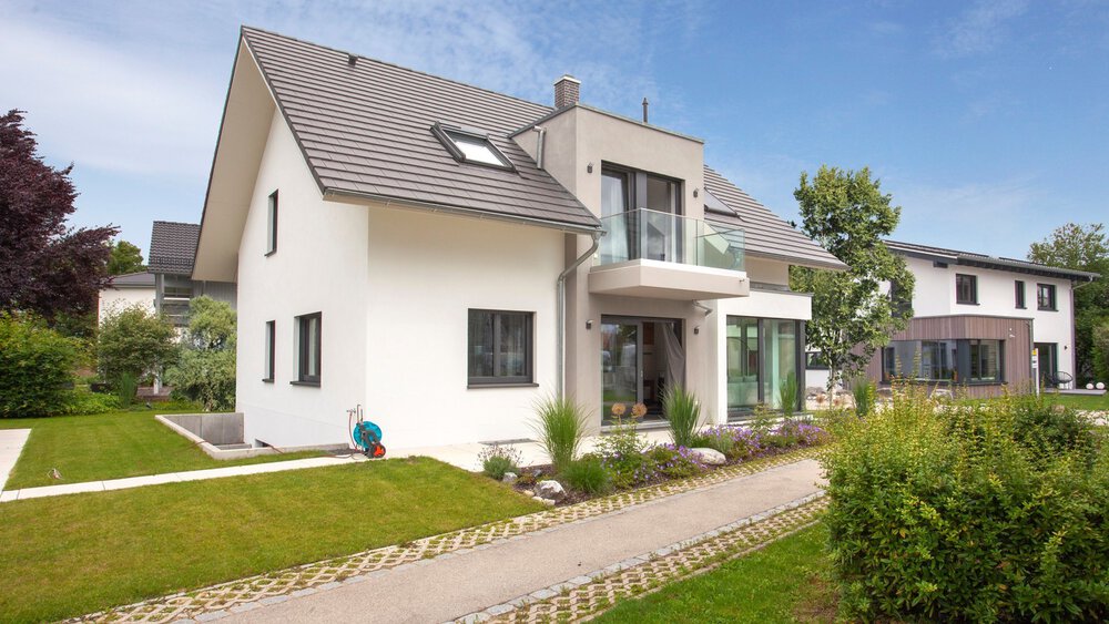 Modernes zweistöckiges Haus mit Satteldach, umgeben von einem Garten und einem Weg, unter einem klaren blauen Himmel.