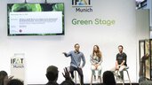 Three people sitting on the IFAT Munich Green Stage presenting,  while the members in the audience raise their hands.