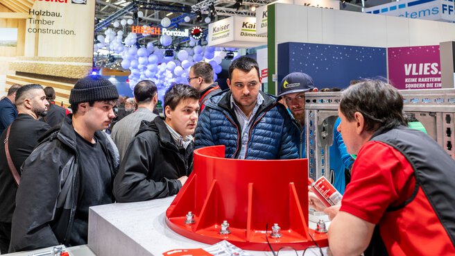 An exhibitor speaks to a group of visitors milling around an exhibit at his stand.