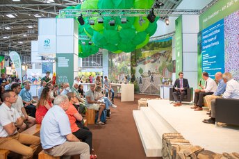 Eine Podiumsdiskussion über europäische Wälder findet auf einer Bühne mit Publikum bei einer Indoor-Veranstaltung statt.