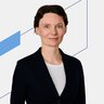 Frau in dunklem Blazer und weißem Hemd vor einem weißen Hintergrund mit blauen geometrischen Linien.
