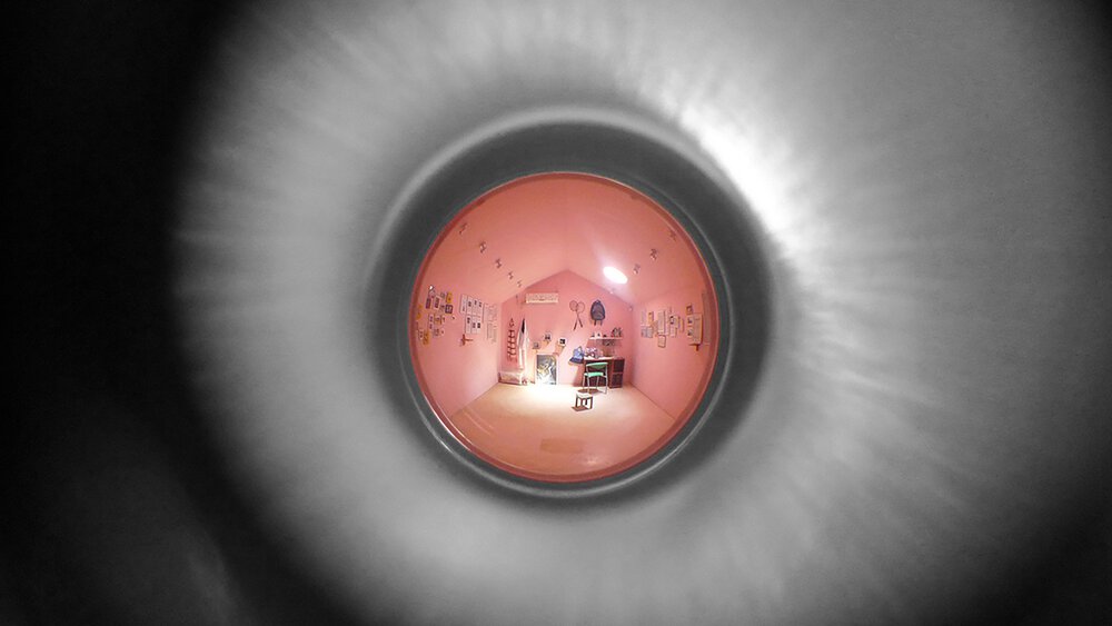 Ein rosa Schlafzimmer, durch ein Guckloch gesehen, umgeben von einem verschwommenen grauen kreisförmigen Rahmen.