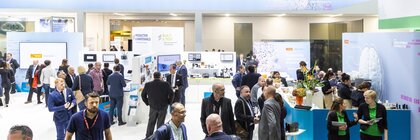 People talking at a technology conference, with displays and stands. At the top of the image is an orange stripe with the URL farnell.com above it.