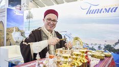 Traditionally dressed man at a Tunisia stand at a travel fair, artfully working sheet metal.