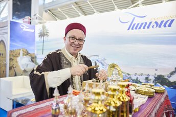 Traditionell gekleideter Mann an einem Tunesien-Stand einer Reisemesse, der kunstvoll Blech bearbeitet.
