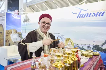 Traditionally dressed man at a Tunisia stand at a travel fair, artfully working sheet metal.