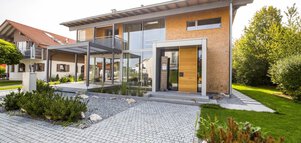 Modernes zweistöckiges Haus mit großen Fenstern, umgeben von Grün und einem gepflegten Garten.