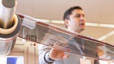 Ein Mann präsentiert eine mit Elektronik bedruckte Folie die von einer Rolle abgewickelt wird.