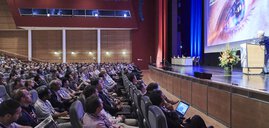 Das Publikum sitzt in einem großen Konferenzraum und verfolgt aufmerksam eine Präsentation auf der Bühne.