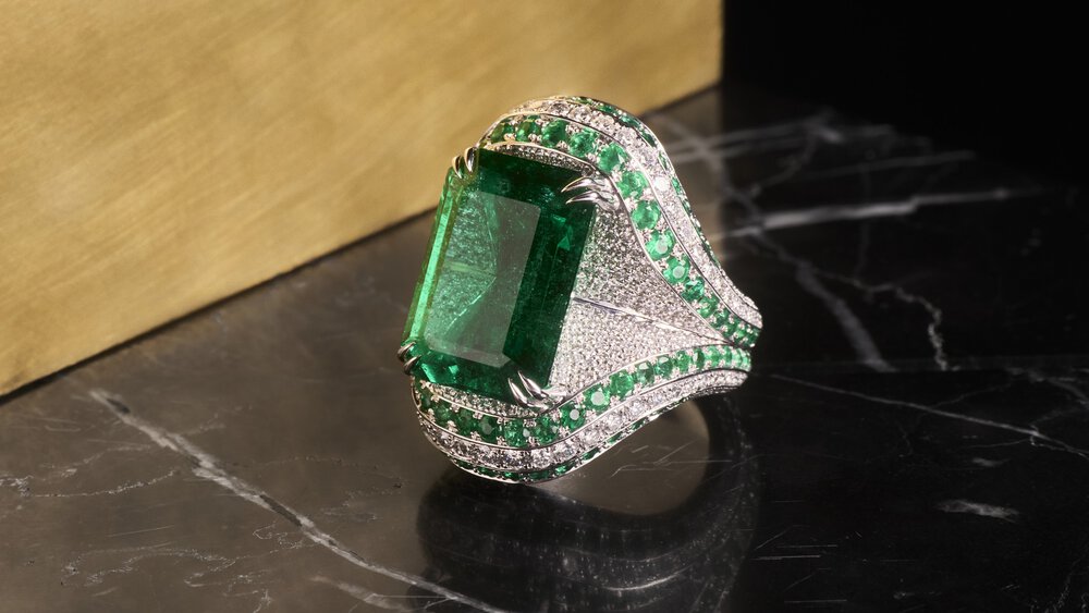 A silver ring with a large emerald gemstone on a dark marble surface.