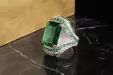 A silver ring with a large emerald gemstone on a dark marble surface.