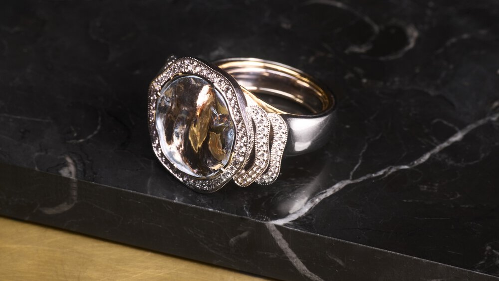 Elegant silver ring with a large clear gemstone and small diamonds on a dark marble surface.