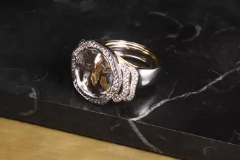 Eleganter Silberring mit einem großen klaren Edelstein und kleinen Diamanten auf einer dunklen Marmoroberfläche.