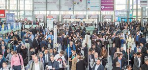 Entrance to the analytica trade fair with many people passing through the turnstiles.