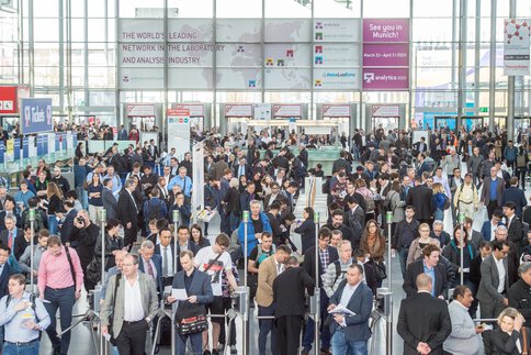 Eingang Messe analytica mit vielen Menschen, die durch die Drehkreuze gehen.
