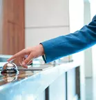 A person in a blue jacket rings a service bell on a counter.