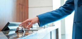 A person in a blue jacket rings a service bell on a counter.