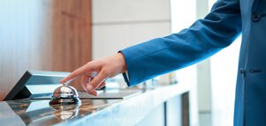 A person in a blue jacket rings a service bell on a counter.