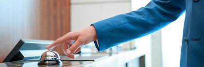 Eine Person im blauen Jacket läutet eine Serviceklingel auf einer Theke.