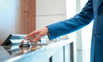 A person in a blue jacket rings a service bell on a counter.