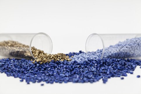 Zwei liegende, offene Reagenzgläser mit blauen und goldenen Körnern, vor einem weißen Hintergrund.
