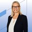 orträt einer Frau mit schulterlangem blonden Haar in dunkelblauem Blazer und weißer Bluse mit kleinem Ausschnitt vor einem hellen Hintergrund mit blauen grafischen Linien